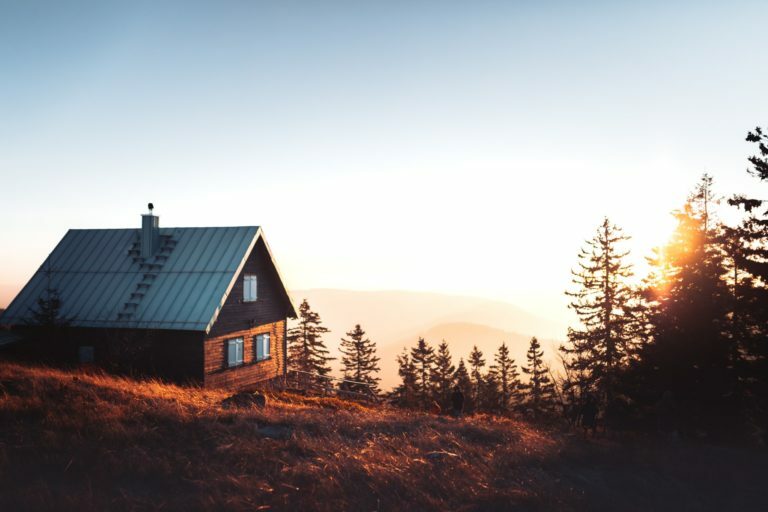 a house on a hill with trees and a sunset in the background