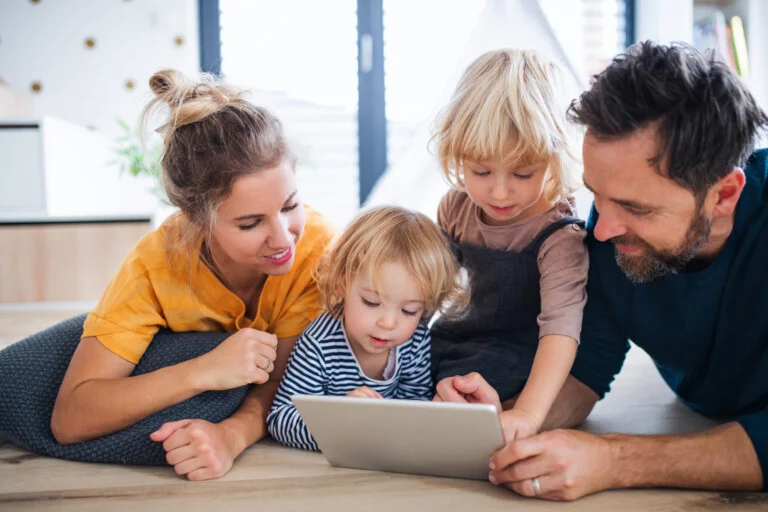 Young family with two small children indoors in bedroom, using tablet.